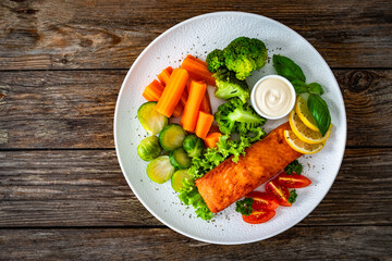 Fried salmon steak with boiled broccoli, brussels sprouts and carrots and mayonnaise on wooden table. Top view