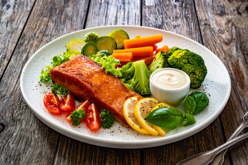 Fried salmon steak with boiled broccoli, brussels sprouts and carrots and mayonnaise on wooden table	
