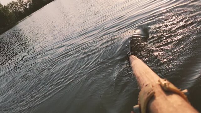 Rowing on summer lake. Camera follows paddle splashing water at sunset