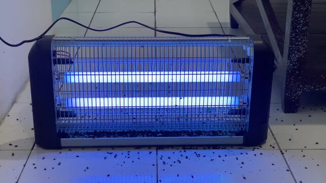 Electric insect killer lamp with dead flies on floor near the device