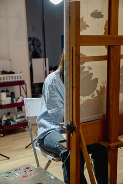 Young woman painting on canvas while sitting at an easel in an art studio. Artistic practice supports creativity, education and skill development.