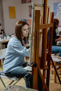 Young woman painting on canvas with an easel in an art studio. Creative process supports education, hobby, self expression and artistic development.