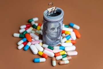 Rolled US dollar bills secured with a clip placed among colorful pills and capsules. High cost of medicine and healthcare expenses, pharmaceutical industry profits concepts.
