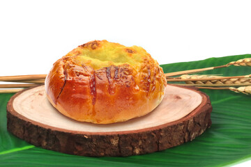 Freshly Baked Golden Custard Bun on Wooden Board with Green Leaf Background