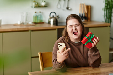 Young woman with Down syndrome celebrates joyfully at home while unwrapping a gift