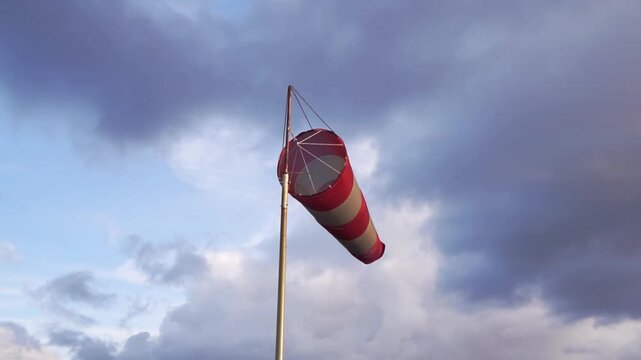 Windsock flutters on a tall mast beneath heavy clouds, showing wind direction and speed in changing weather. Aviation and meteorology symbol with moody light and ample copy space