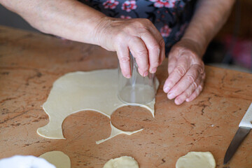 Person using circle cutter on rolled dough at wooden table. Ideal for cooking tutorial closeup, dumpling making guide, culinary blog content or homemade food preparation poster template.