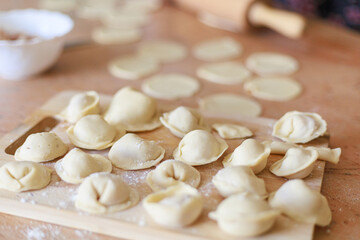 Homemade dumplings neatly arranged on wooden board in cozy authentic kitchen. Concept of food preparation, tradition, and family warmth with copy space.