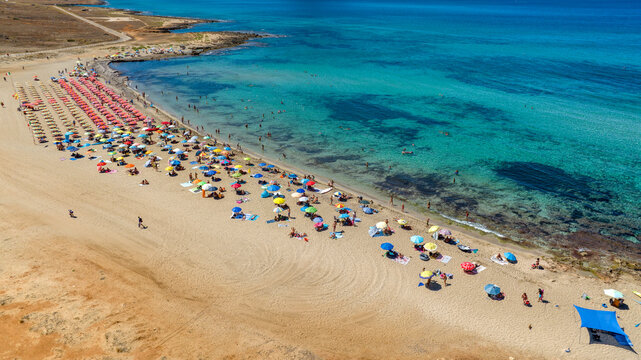 Aerial view of Macari Beach located near San Vito Lo Capo, in province of Trapani, Sicily, Italy. Many vacationers with umbrellas bathing in the clear, turquoise sea. There's a beautiful beach club.