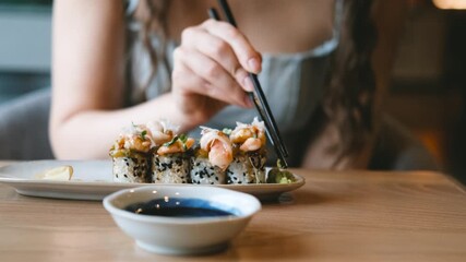A beautiful girl eats Japanese sushi rolls with chopsticks, smiling with pleasure