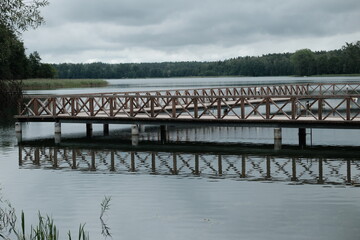 Drewniane molo na jeziorze Ołów, Mazury, spokojna woda i odbicie pomostu w jeziorze © Przemysaw