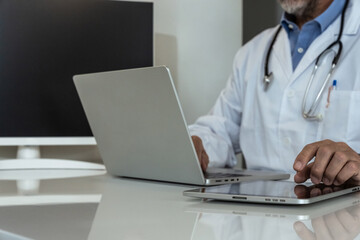 Dedicated doctor in a clinic setting, working with a tablet and laptop, symbolizing modern medical practice