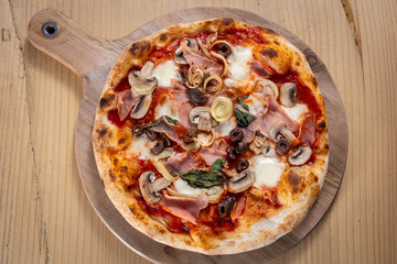 Freshly Baked Italian Pizza with Ham, Mushrooms, Olives and Mozzarella on Wooden Board. Traditional Homemade Recipe, Authentic Pizzeria Style, Delicious Mediterranean Food Concept