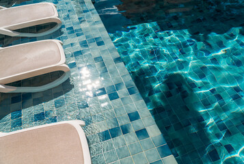 Sunlit sparkling blue pool water next to stylish lounge chairs on tiled edge, embodying tropical holiday, luxury resort, and relaxing summer leisure for travel and lifestyle uses.