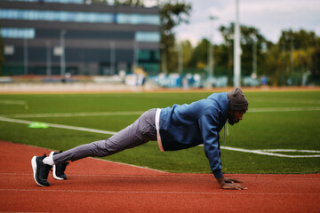 Determined African American male athlete performs a plank or push-up exercise on a running track as part of his strength training and core workout