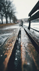 Wet wooden bench in a park during early winter, with distant figures and bare trees