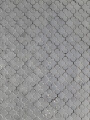 Dark gray asphalt or rubber floor covering with a detailed, repetitive circular geometric pattern. Abstract background and deep texture suitable for industrial, urban, and modern design themes.