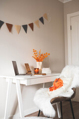 autumn workplace desk decorated with chair with autumn decor on pillow, notebook, note candle, vase...