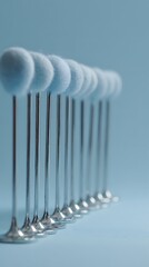 A delicate row of soft, light blue pom-poms on slender silver stands creates a charming, minimalist aesthetic perfect for design projects.