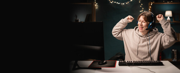 E-sport female gamer in headphones play online video game doing winner gesture celebrate clenching...