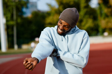 Close-up of an male athlete clenching his teeth in pain while holding his injured arm or forearm during a workout break on a running track.