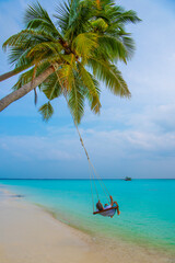Tranquil closeup calm sea water waves with palm trees. Man tourist swinging, Tropical island beach landscape exotic shore coast. Summer vacation, holiday amazing nature. Relax paradise, Maldives.