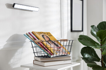 Stylish LED lamp on white wall, stool with books and magazines indoors