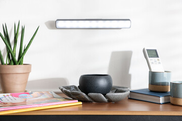 Stylish LED lamp on white wall above wooden table with magazines and decor indoors