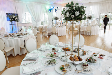 Elegant wedding banquet hall interior showing a beautifully set dinner table with a floral centerpiece, white chairs, and drapery, ready for guests to arrive for the celebration
