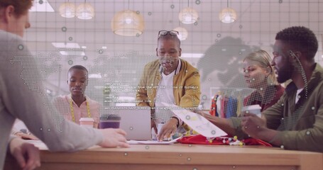 Collaborating coworkers examining fabric swatches at studio table, with measuring tape and laptop