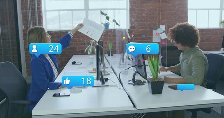 Office workers discussing printed report between dual monitors in office, with social media icons