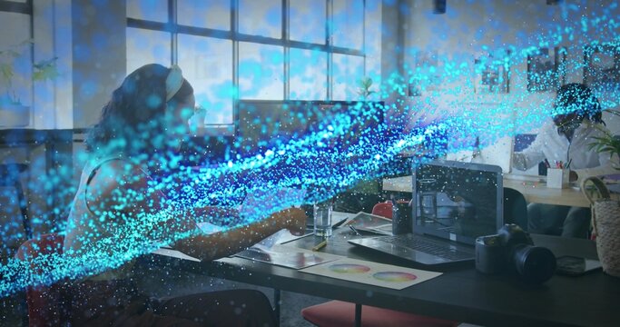 Woman reviewing color charts on laptop in open-plan office, with DSLR camera and glass of water - Powered by Adobe