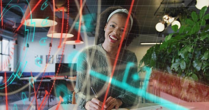 Writing office worker wearing sweater at open-plan desk, using pen on notebook with overlaid charts