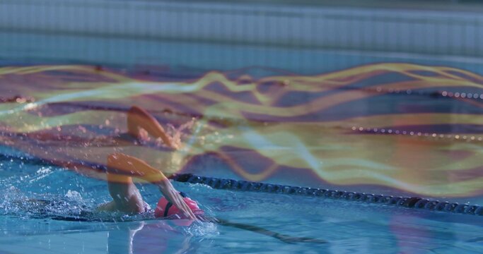 Performing backstroke, woman gliding in pool lane, with goggles pink cap swimsuit light trails