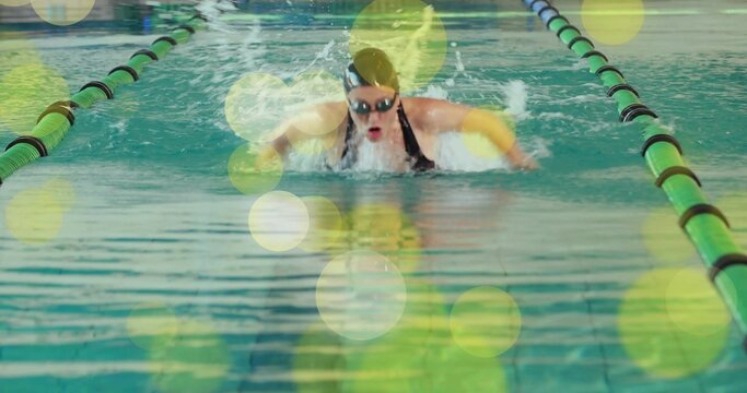 Performing butterfly stroke swimmer wearing goggles and yellow armbands in pool lane with dividers