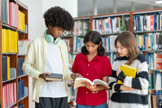 Group of diverse teenagers standing in library, reading books together and discussing information in book at school. Learning, knowledge, and education concepts.