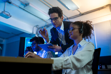 Businessman coaching and training woman customer service agent wearing headsets support and assistance to clients working in call center office at night.