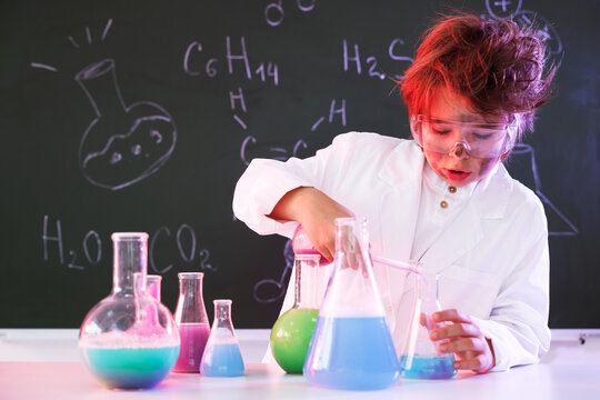Back to school. Boy doing chemical research at desk against chalkboard with formulas indoors