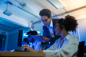 Businessman coaching and training woman customer service agent wearing headsets support and assistance to clients working in call center office at night.