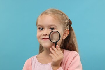 Little girl with magnifying glass on light blue background