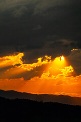 Golden sunlight piercing dark storm clouds during sunset over Carpathian mountains