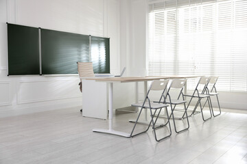 Green chalkboard and stylish furniture in classroom. Mockup for design