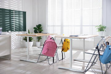 Green chalkboard, desks and chairs with backpacks in classroom