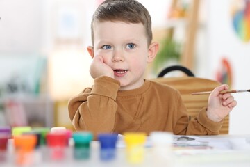 Cute little boy with brush drawing at white table indoors