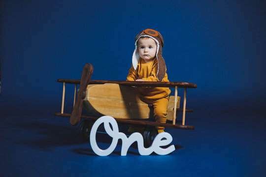 Little aviator celebrates first birthday with a charming outfit and toy airplane under a vibrant blue backdrop, creating a delightful scene full of joy and wonder