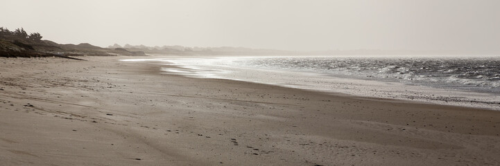 Brouillard marin poussé par le vent vers la côte, lumière diffuse, plage déserte.
