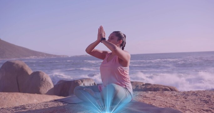 Meditating woman wearing sportswear sitting at rocky coast, with yoga mat and fitness tracker - Powered by Adobe