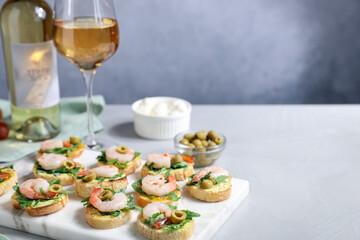 Delicious bruschettas with shrimps and wine on light table. Space for text
