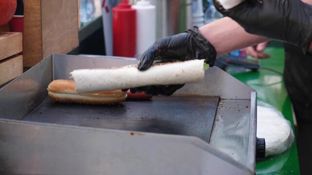 Close-up of street cafe worker's hands in black gloves flipping a filled wrap roll on griddle during doner kebab fast food preparation service