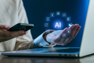Hands holding a smartphone and interacting with AI technology on a laptop in a modern workspace